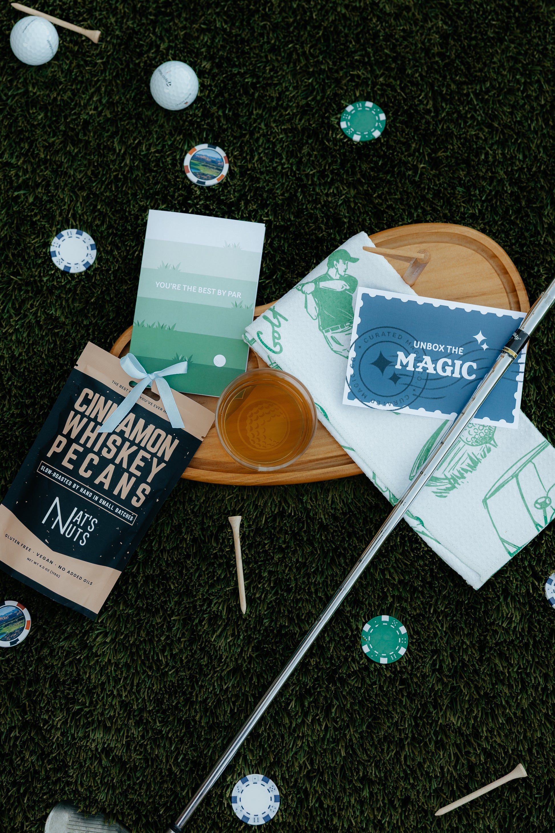 Golf Themed charcuterie board with cinnamon whiskey pecans, golf towel, best by par card and drink. Card saying unbox the magic
