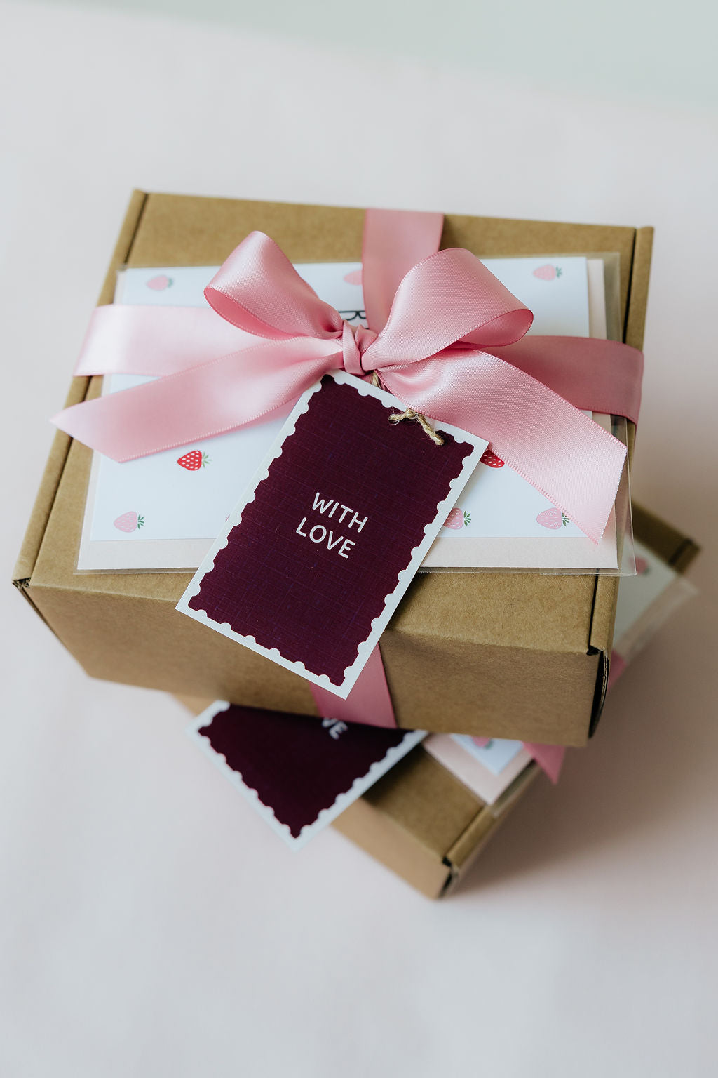 Gift box with a pink ribbon and 'With Love' card on a light background