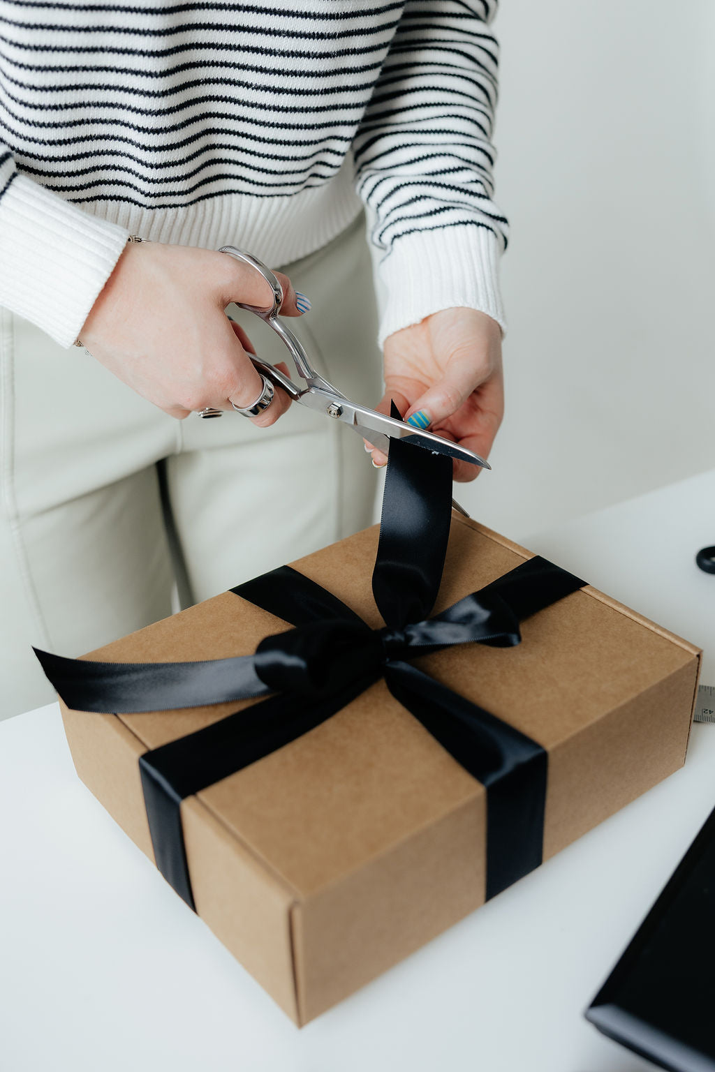 Person cutting a brown gift box with a black ribbon using scissors.