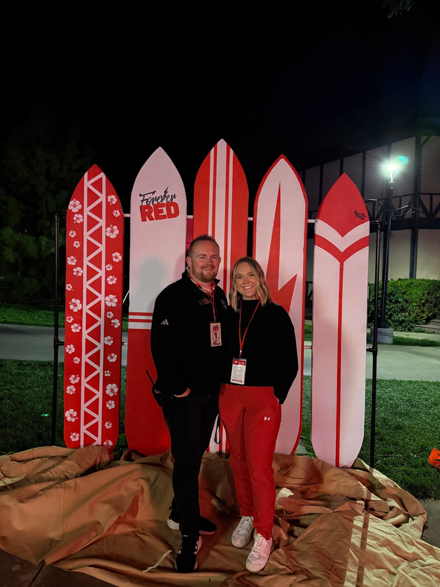 Kenten & Paige standing in front of decorative surfboard props at night.