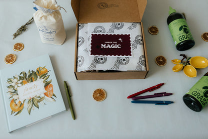 Box labeled 'Unbox the Magic' with a notebook, pen, and decorative items on a white surface.