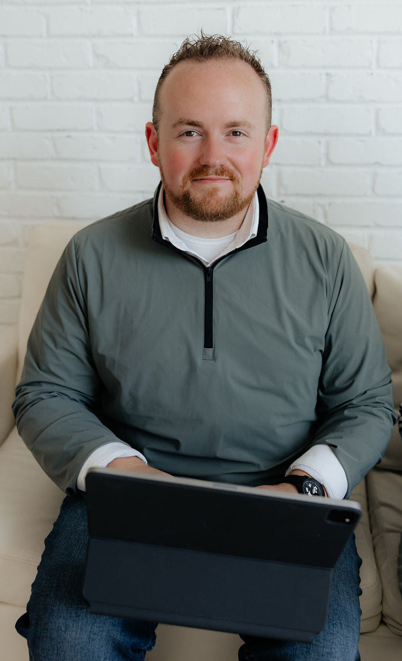 Kenten sitting on a couch holding a tablet with a white brick wall background