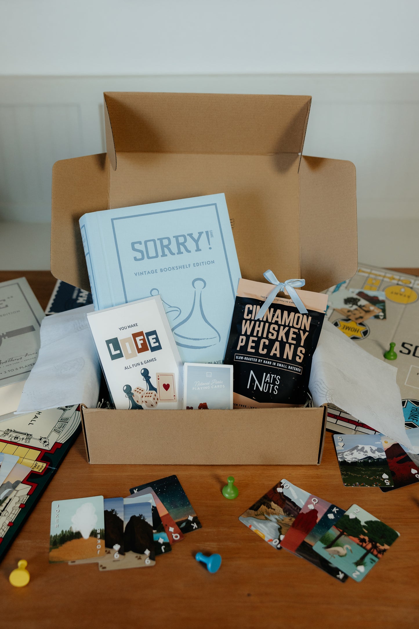 Open cardboard box with various items including a game titled 'SORRY!', a box of cinnamon whiskey pecans, and other small products on a wooden surface.