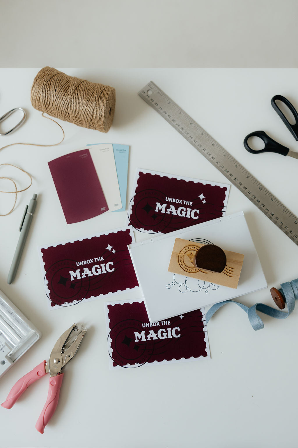 Crafting materials including fabric pieces with 'Unbox the Magic' text, scissors, thread, and tools on a white surface.
