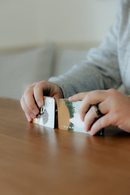 Person shuffling cards with nature-themed designs on a wooden surface.